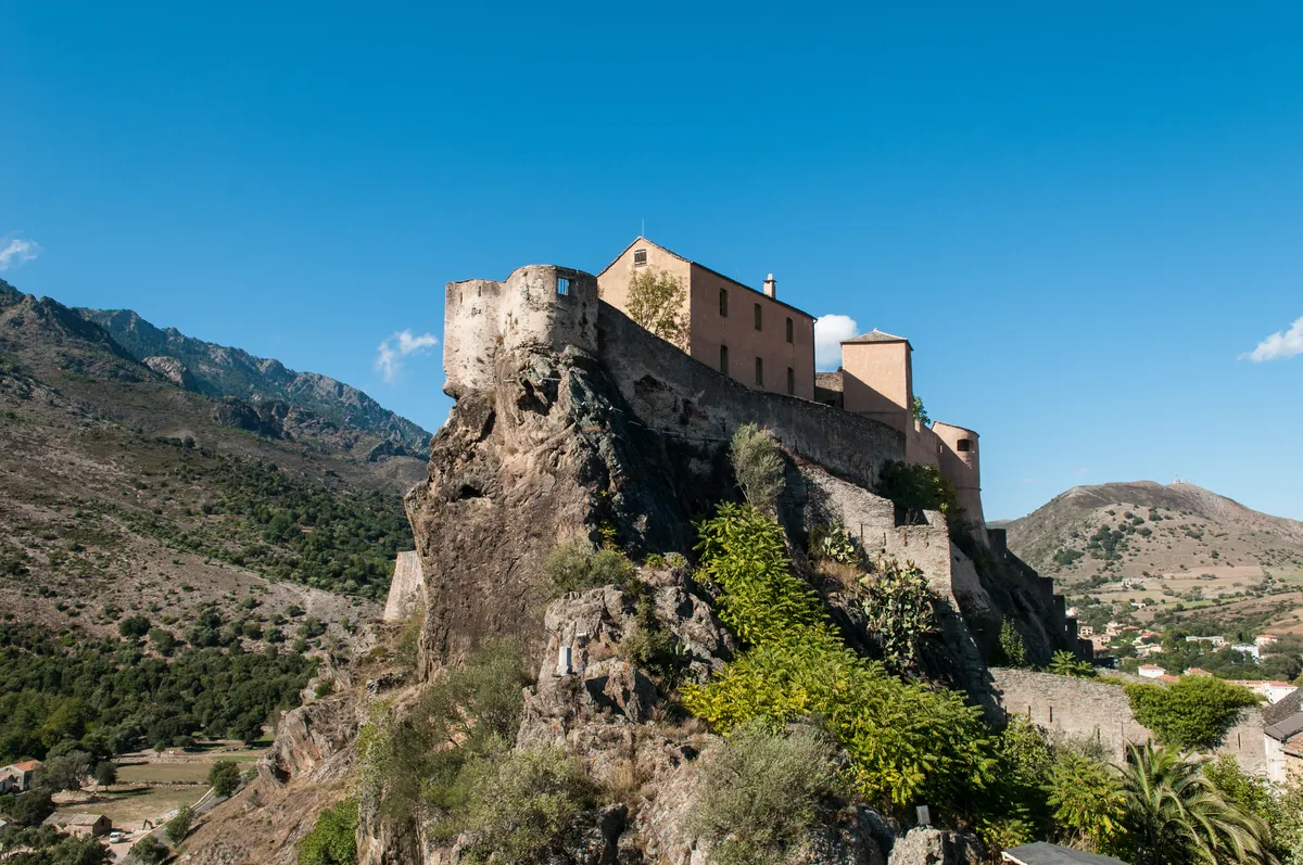 La citadelle de Corte perchée sur son piton rocheux, les montagnes derrière, sous un ciel bleu