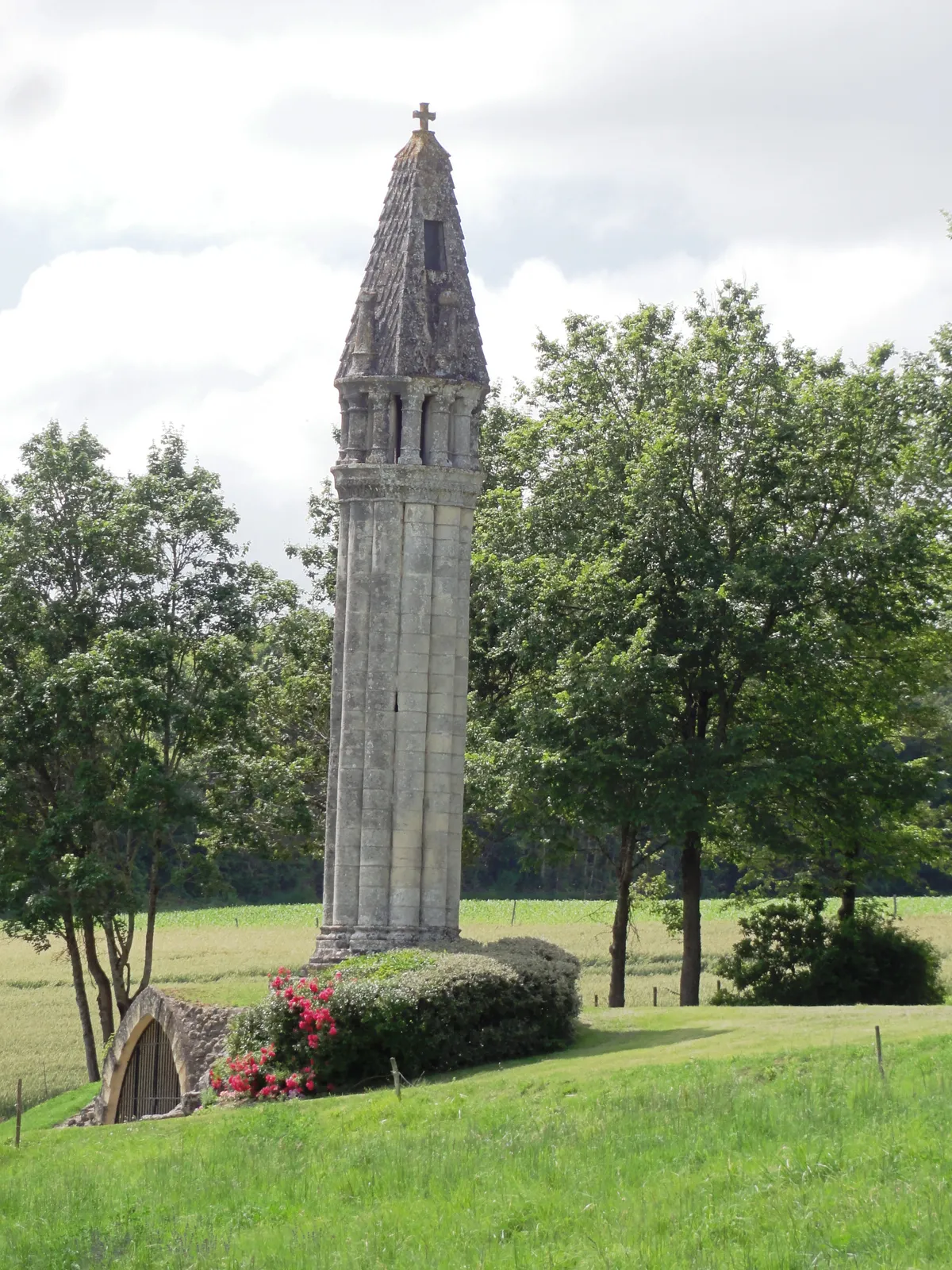 La lanterne des morts de Fenioux, haute tour de pierre faite de colonnettes et coiffée d'un toit pointu, dans un pré bordé d'arbres