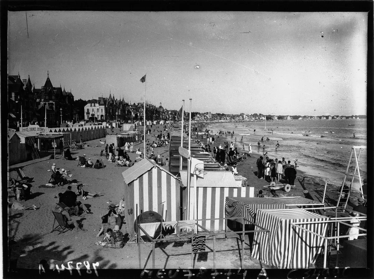 La plage de La Baule en 1930 : des cabines rayées, des baigneurs sur le sable et, derrière, les villas du front de mer