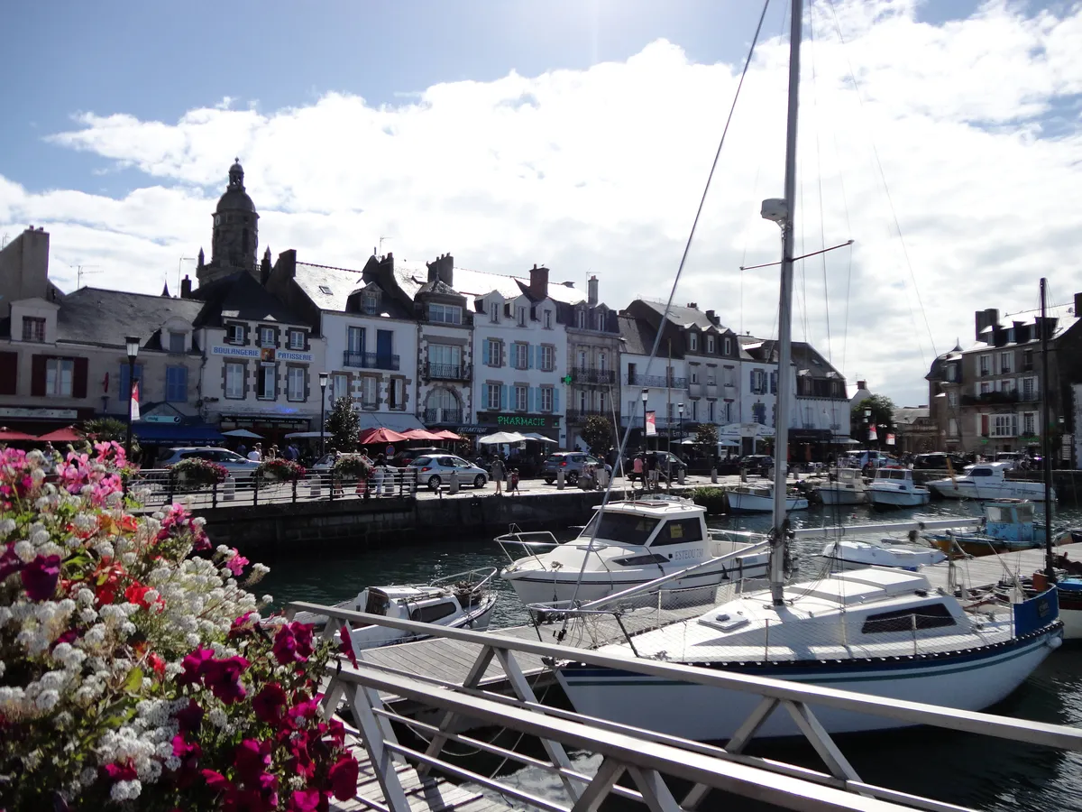Les quais du Croisic, leurs maisons et le clocher de Notre-Dame-de-Pitié, derrière les bateaux du port et des jardinières fleuries