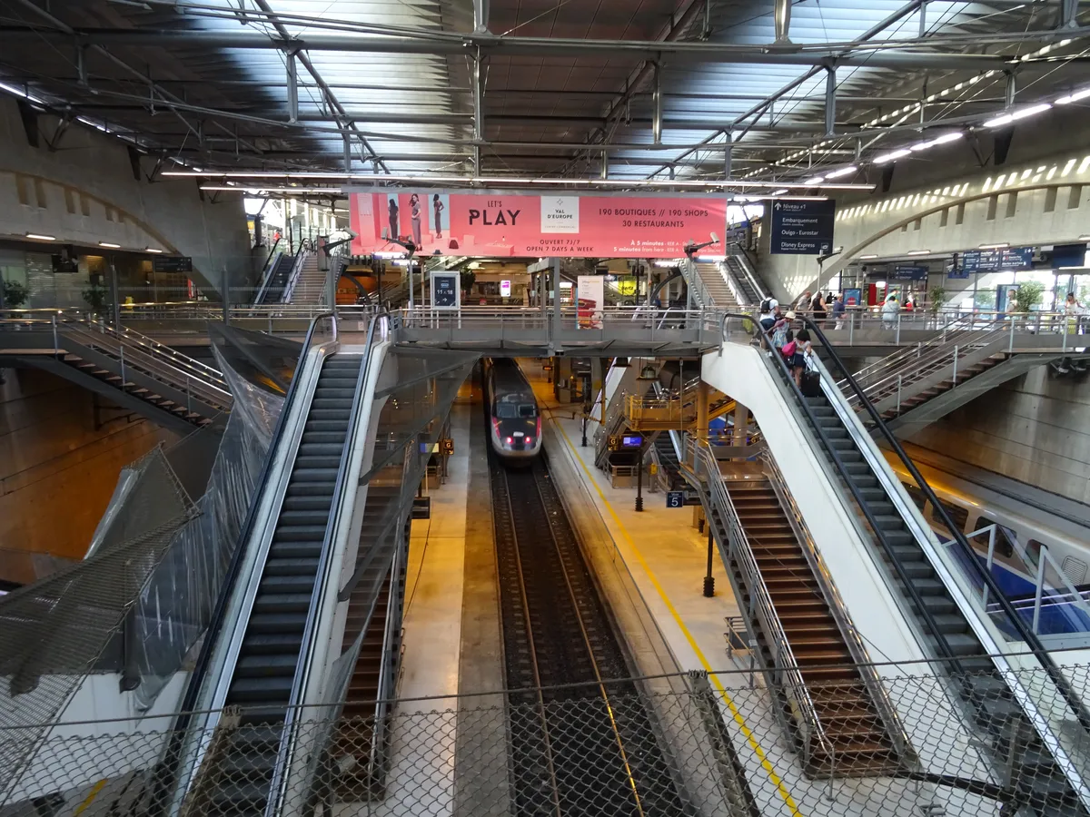 Les quais de la gare de Marne-la-Vallée - Chessy, ses escaliers mécaniques et un TGV à quai