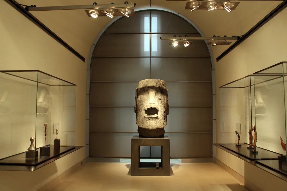 Une tête de moaï de l'île de Pâques exposée entre deux vitrines, au pavillon des Sessions du Louvre