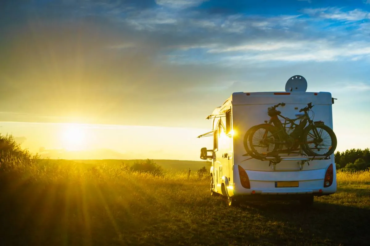 Un camping-car chargé de deux vélos, garé dans un pré face au soleil couchant