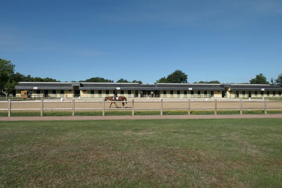 La carrière d'honneur de l'École nationale d'équitation et ses écuries, un cavalier au loin