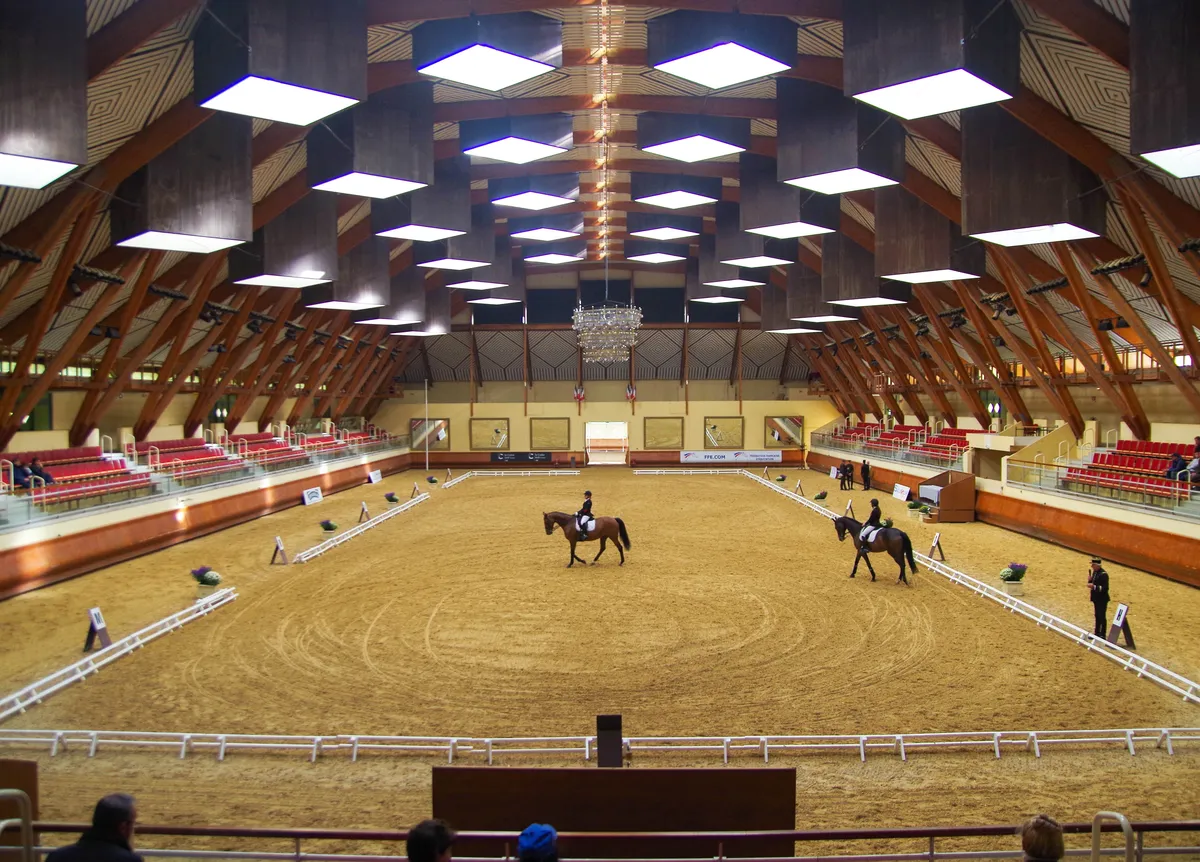 Le grand manège des écuyers du Cadre Noir, sa charpente de bois et deux cavaliers au travail sur la piste